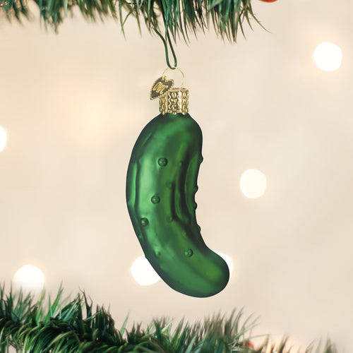 Green pickle-shaped Christmas ornament hanging on a tree with lights in the background.