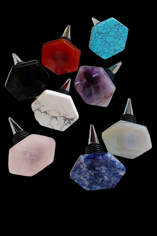 Set of colorful gemstone-shaped bottle stoppers on a white pebble background