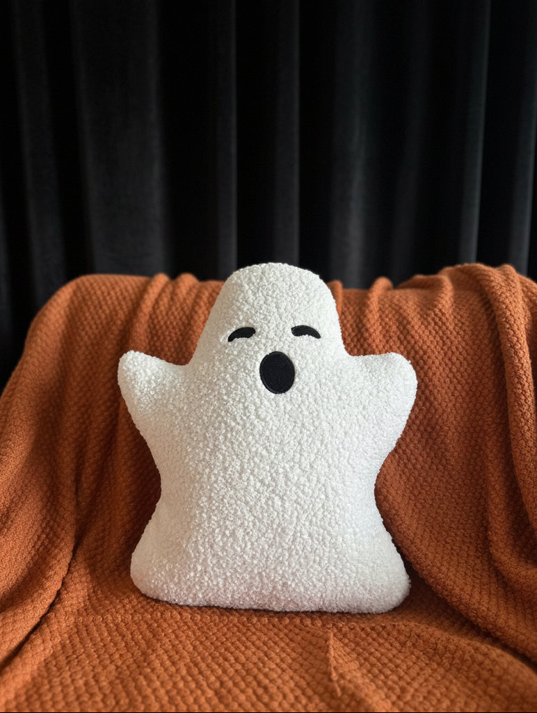 White ghost-shaped pillow with black eyes and mouth on a brown blanket
