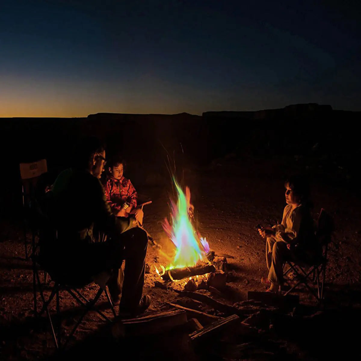 People sitting around a campfire in a desert landscape at night.
