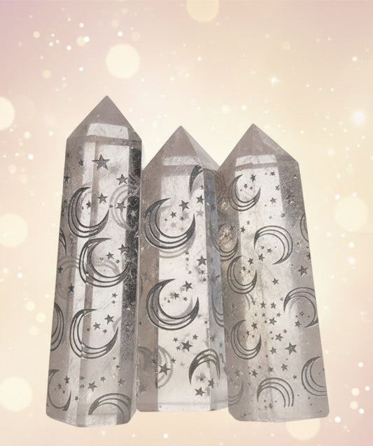 Three crystal points with moon and star patterns held in a hand against a blurred background