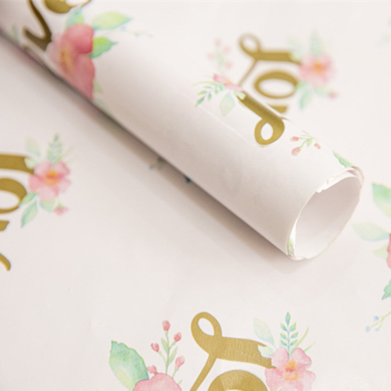 Roll of decorative paper with floral and gold lettering design on a white background