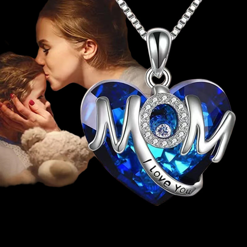 Necklace with blue heart pendant and 'I Love You Mom' text, featuring a blurred background of a woman and child.