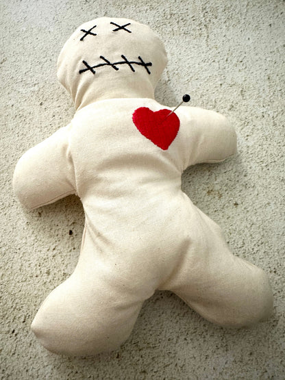 White voodoo doll with red heart and black stitches on a textured surface