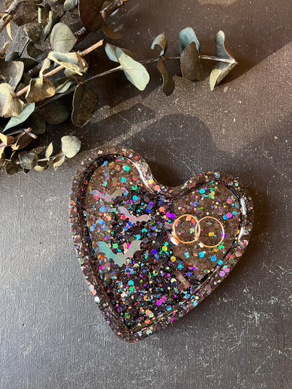 Heart-shaped object with glittery finish on a dark surface with eucalyptus leaves.