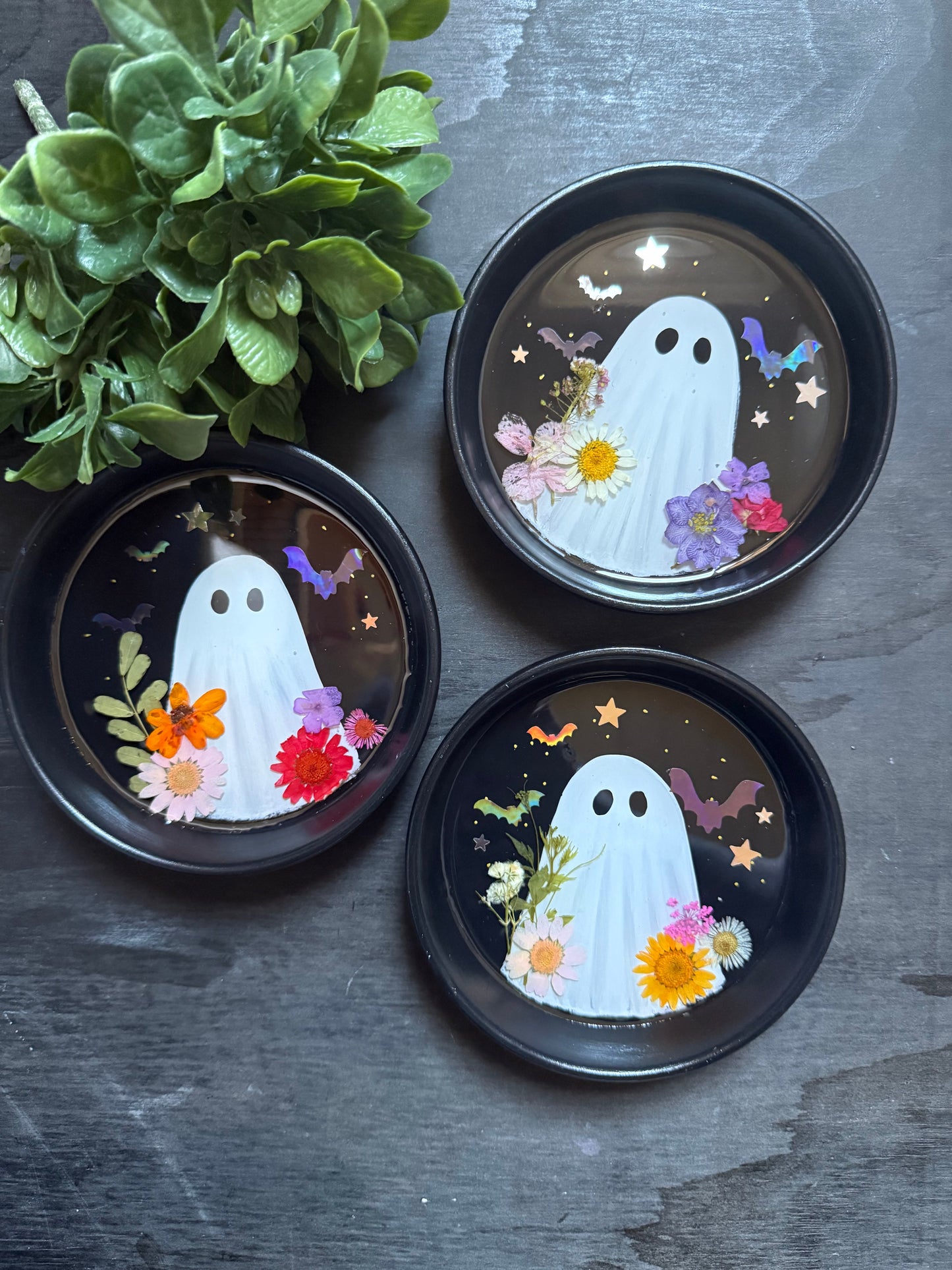 Three decorative plates with ghost designs and flowers on a dark surface.