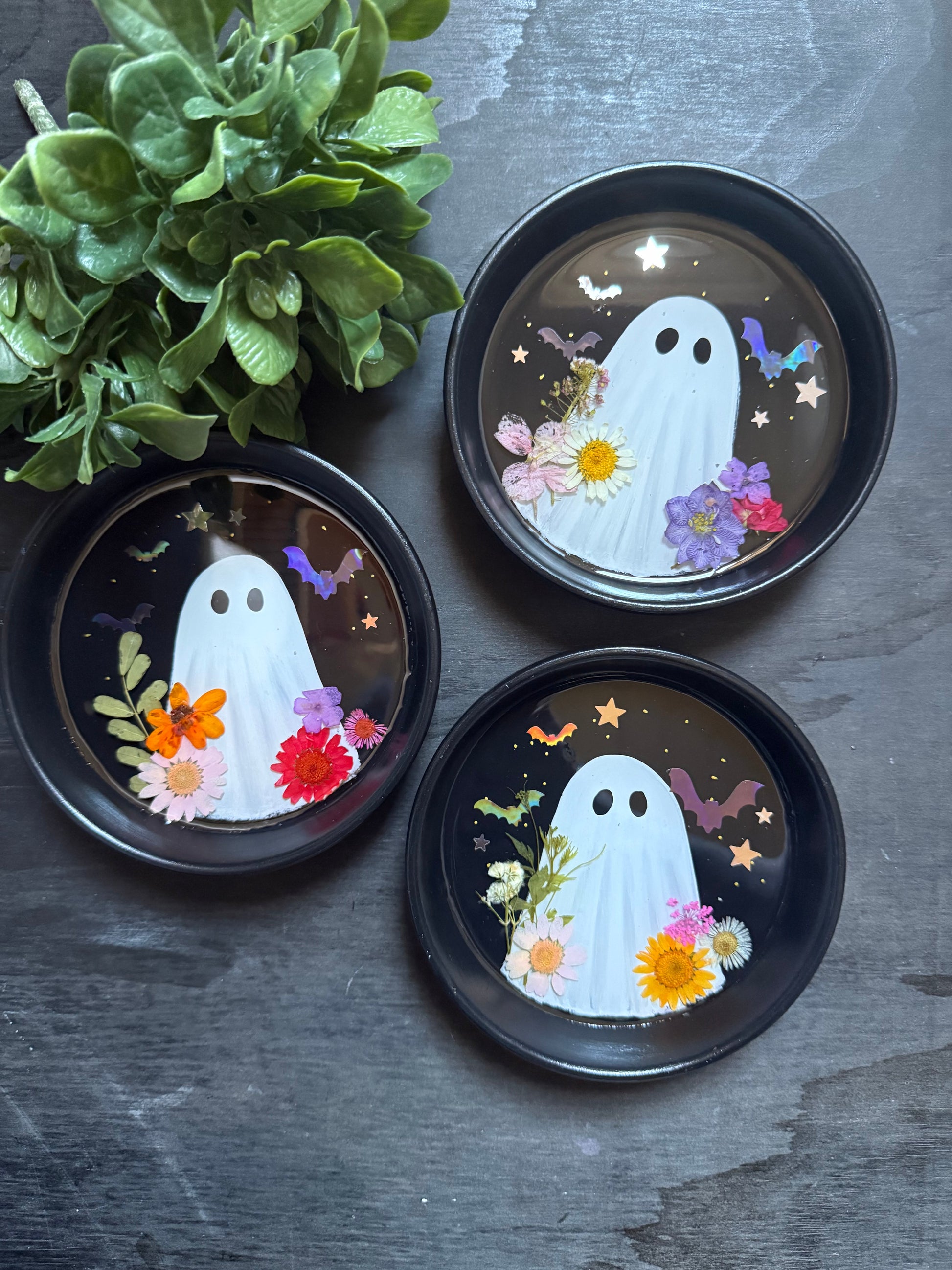 Three decorative plates with ghost designs and flowers on a dark surface.