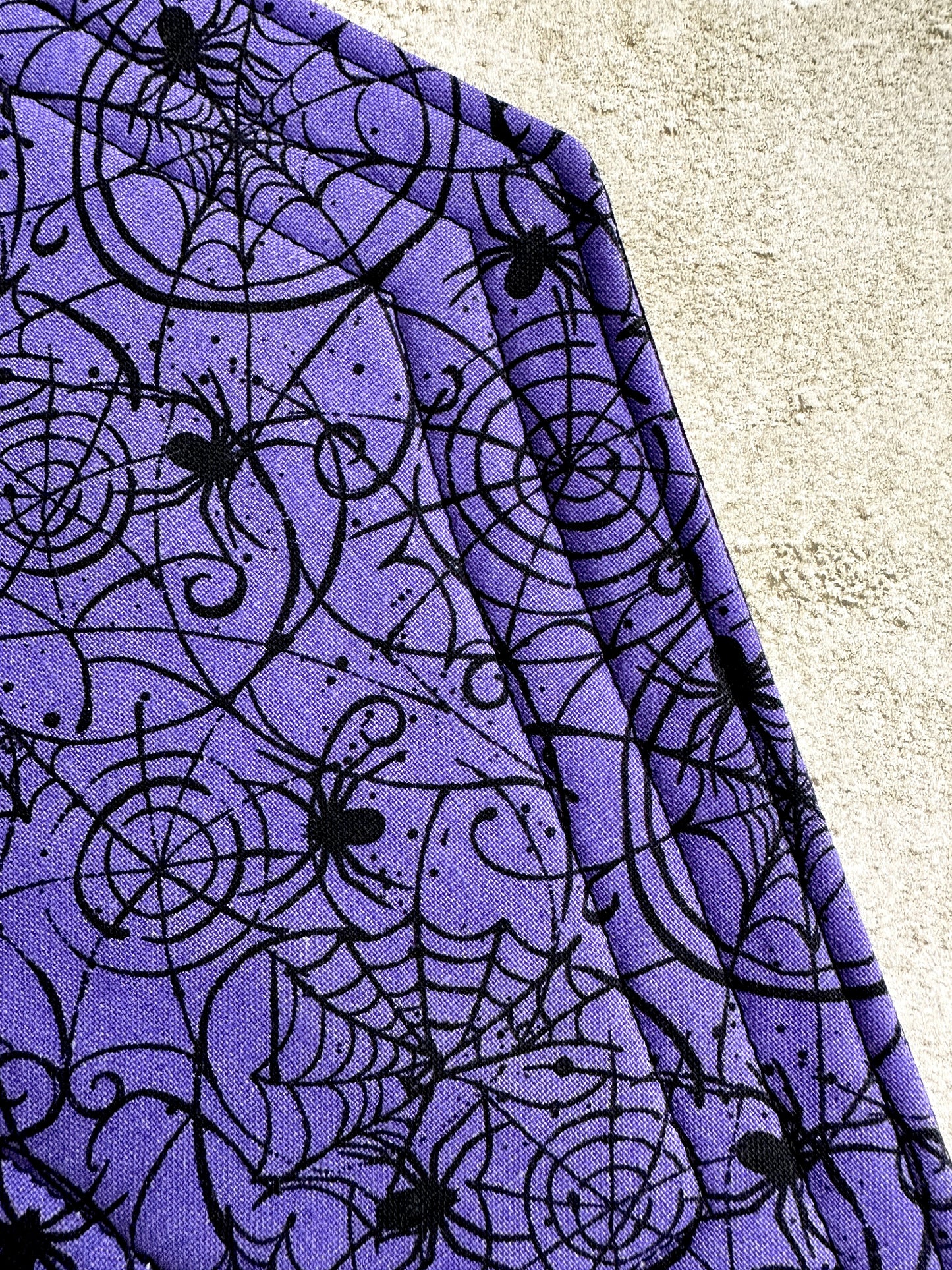 Purple fabric with black spider web and spider pattern on a textured surface