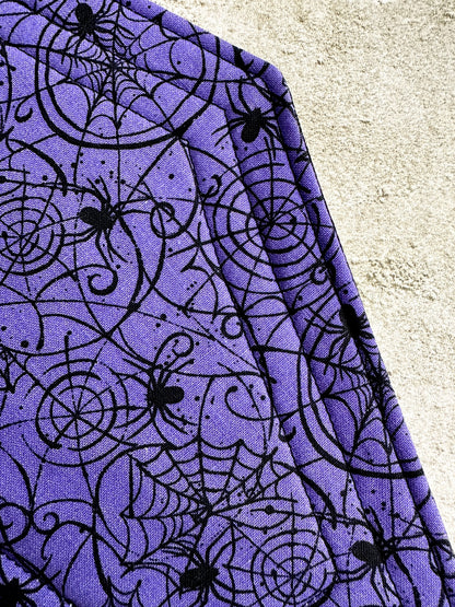 Purple fabric with black spider web and spider pattern on a textured surface