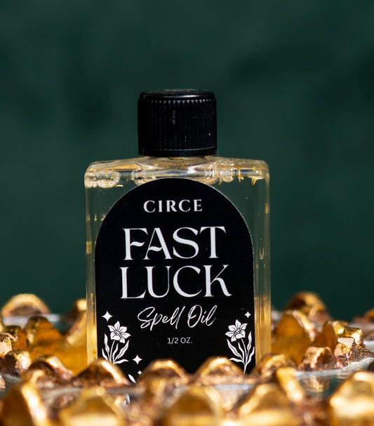 Bottle of Circe Fast Luck Spell Oil surrounded by gold coins on a dark background