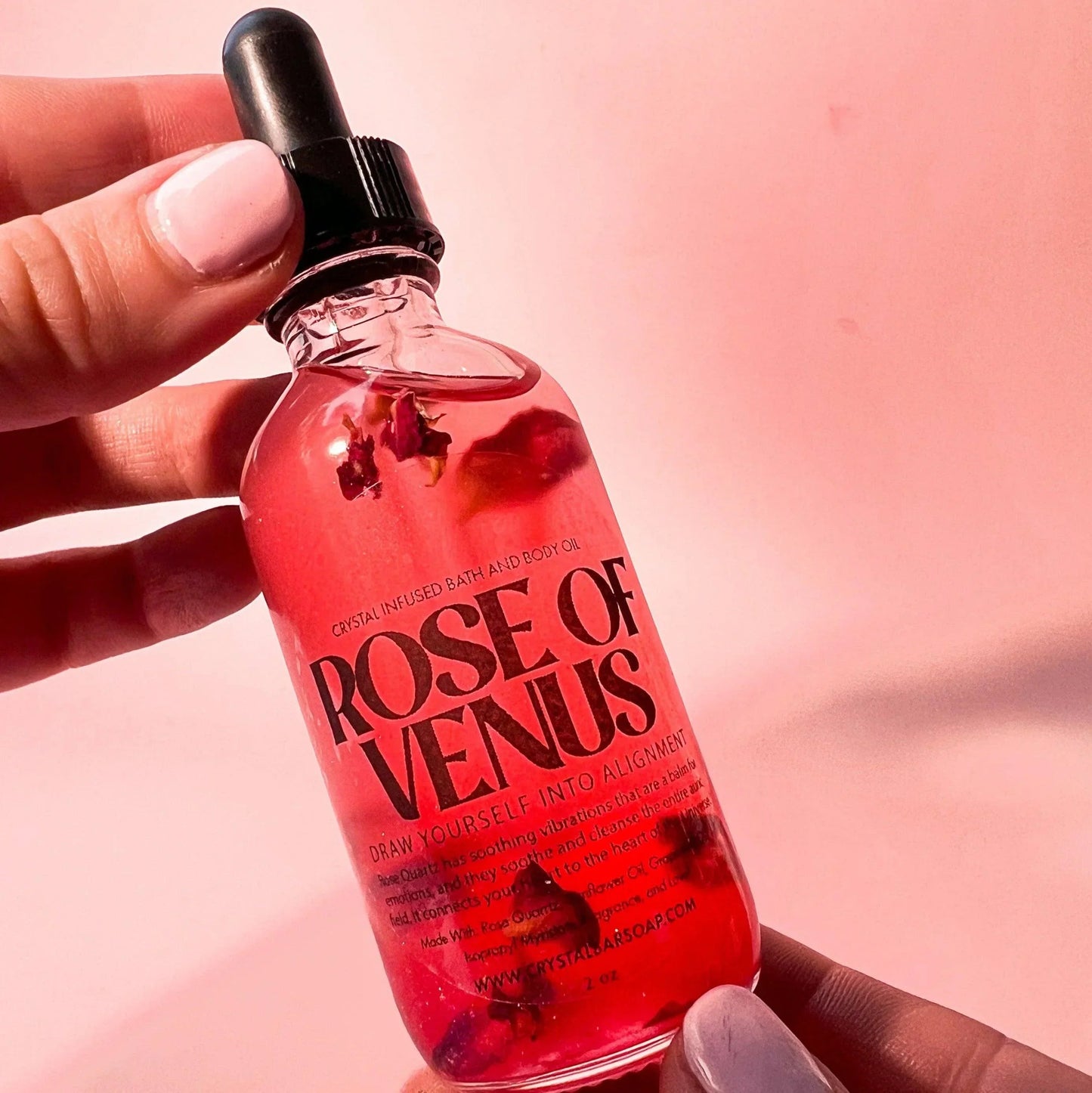 Bottle of 'Rose of Venus' with a dropper held by a hand against a pink background