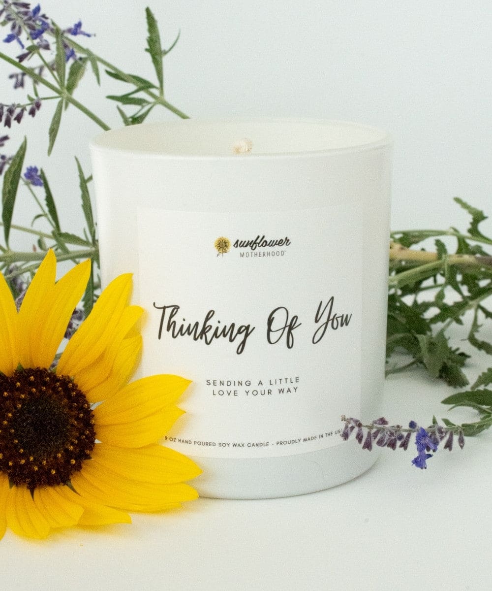 Candle with 'Thinking Of You' text, sunflower, and lavender flowers on a white background