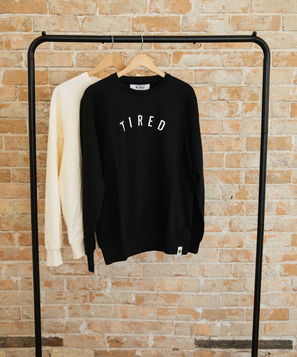 Black sweatshirt with 'TIRED' text on a rack against a brick wall.