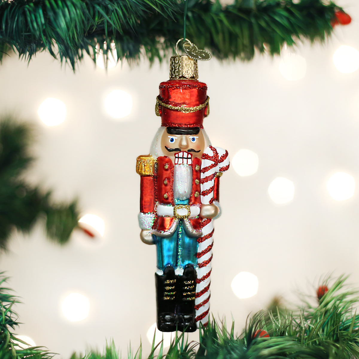 Decorative nutcracker ornament hanging on a Christmas tree with lights in the background.
