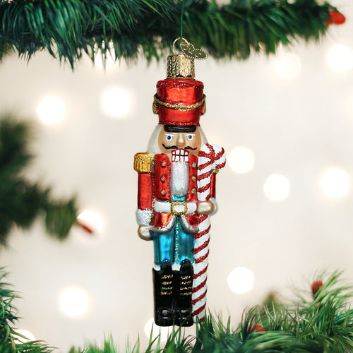 Decorative nutcracker ornament hanging on a Christmas tree with lights in the background.