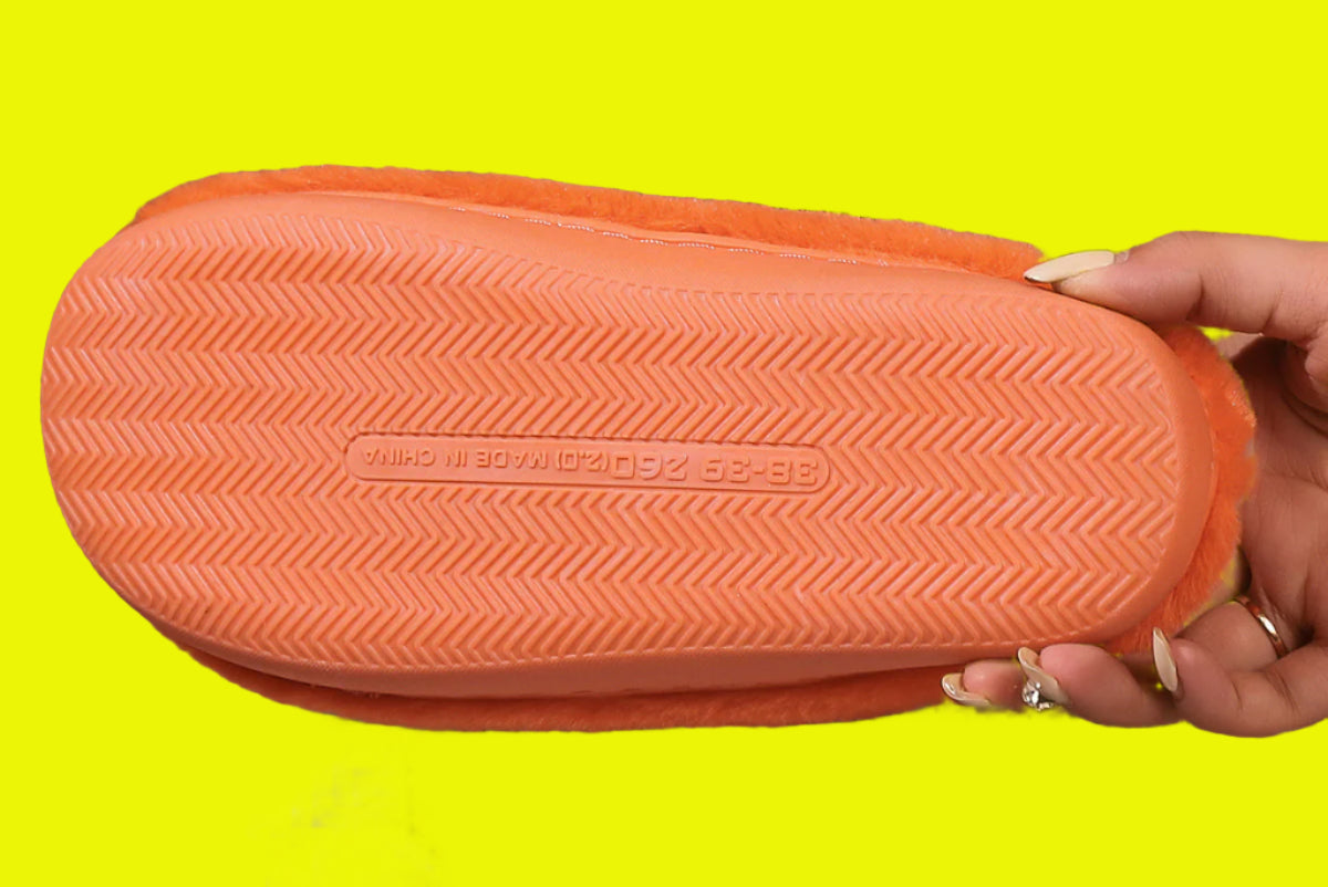 Orange sandal with textured sole held by a hand on a wooden surface