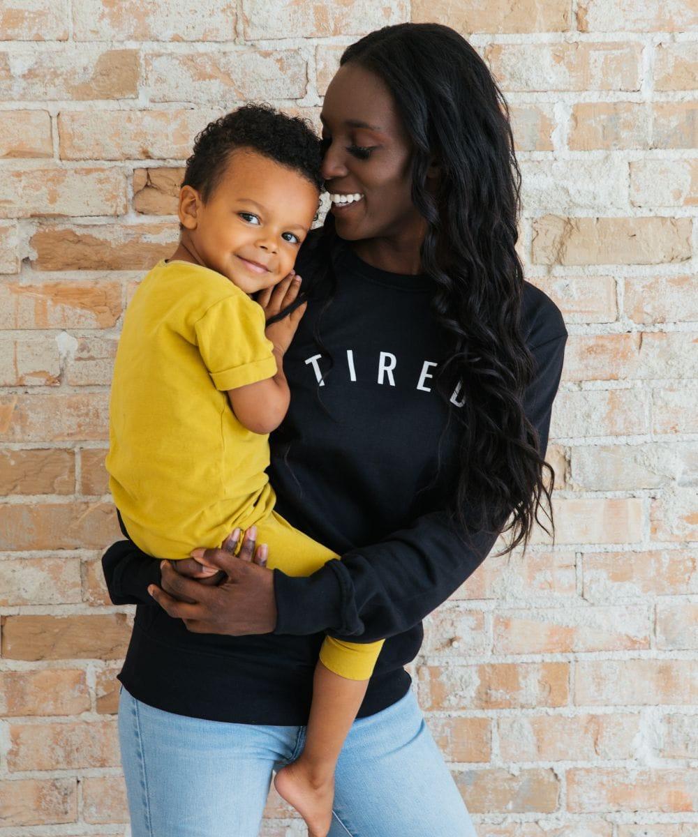 Woman holding a child against a brick wall, both wearing black sweatshirts.