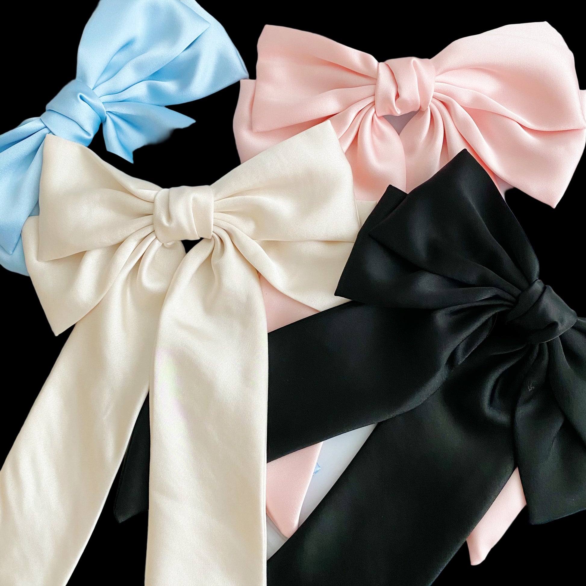 Four satin ribbons in blue, pink, beige, and black on a light gray background