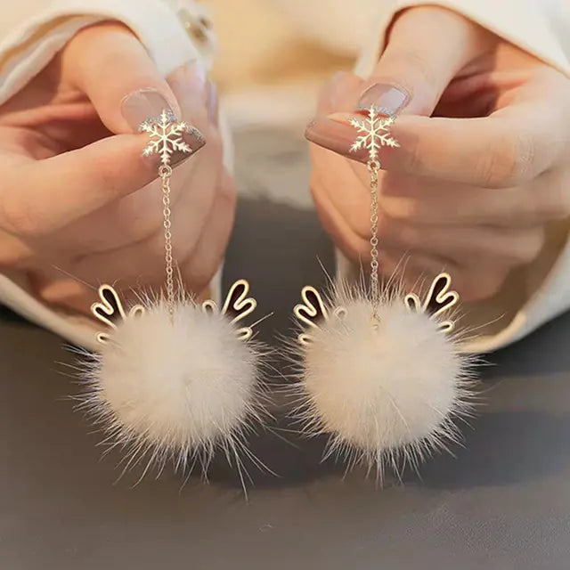 Pair of earrings with fluffy white balls and gold chains held by hands.