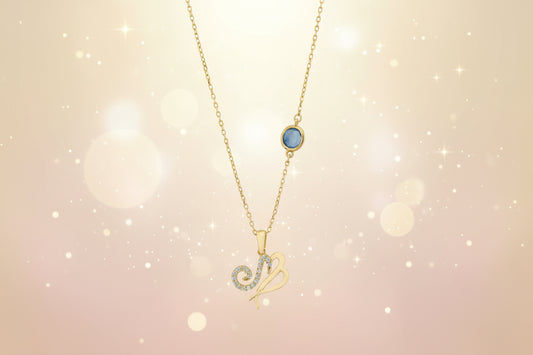 Gold necklace with a blue gemstone and zodiac symbol pendant on a white background