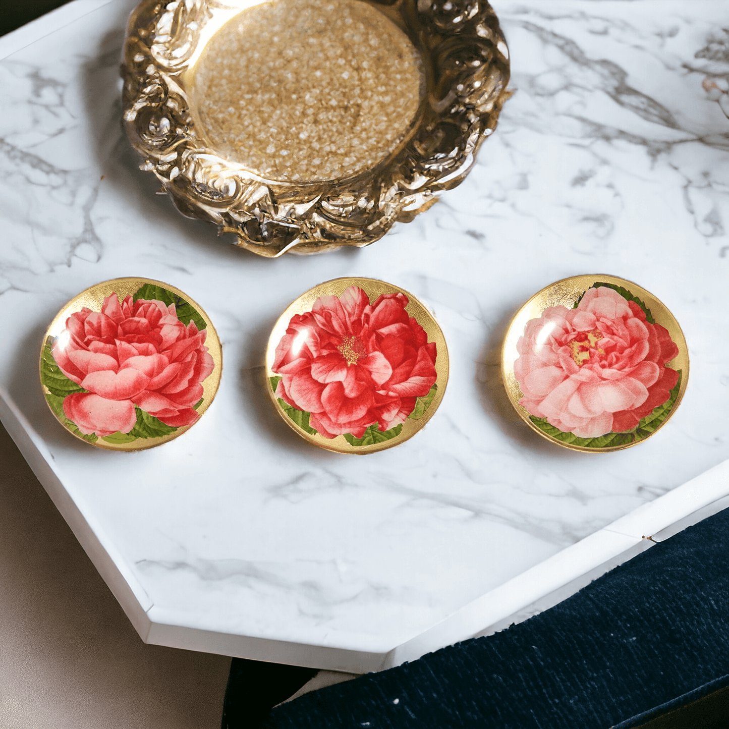 Three floral earrings on a marble surface with a gold dish.