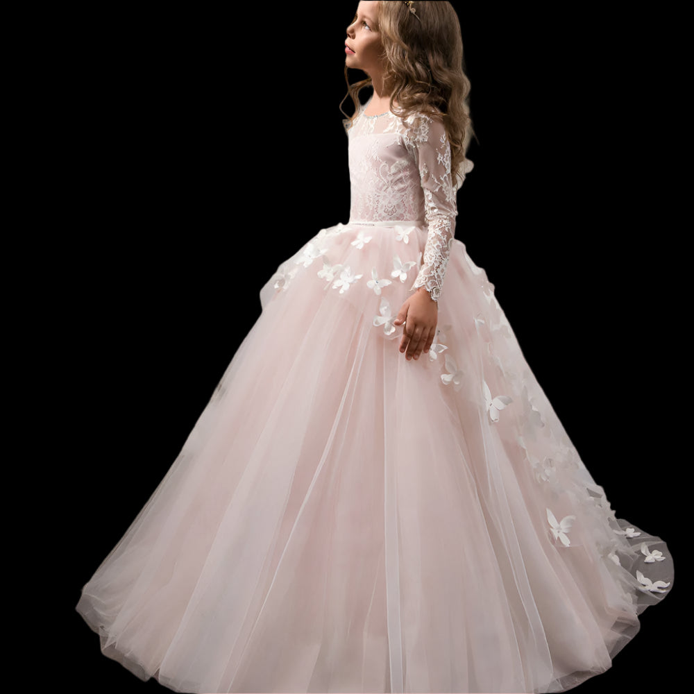 Young girl in a pink floral dress standing in a room with white curtains and a mirror.