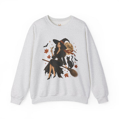 A light heather gray crewneck sweatshirt featuring a large graphic print of a witch riding a broomstick, surrounded by black cats, bats, autumn leaves, and a cat hat.