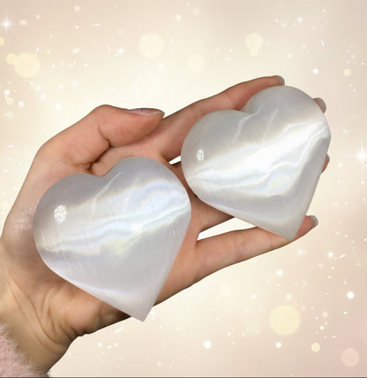 Hand holding two white stone hearts against a dark background