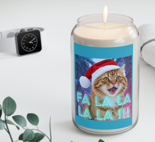 Candle with a cat wearing a Santa hat and 'Fa La La' text on a blue background, placed on a white surface with a plant and watch in the background.