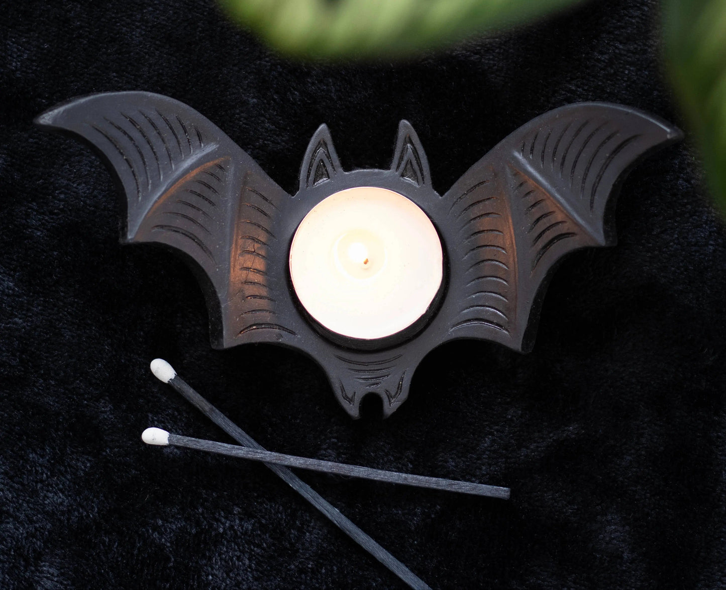 Bat-shaped candle holder with a lit candle on a dark surface
