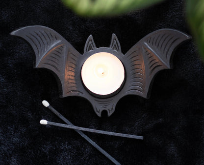 Bat-shaped candle holder with a lit candle on a dark surface