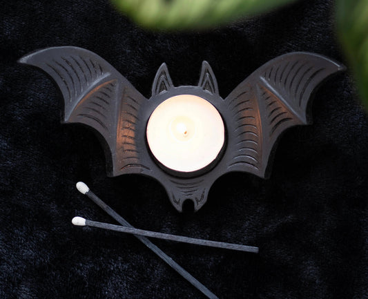 Bat-shaped candle holder with a lit candle on a dark surface