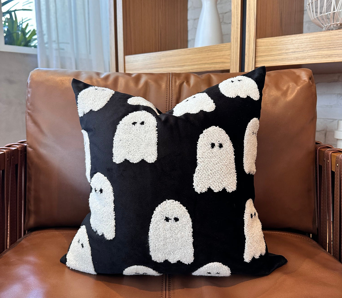 Black pillow with white ghost patterns on a brown leather chair