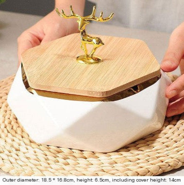 White container with wooden lid and gold deer figurine on a woven mat