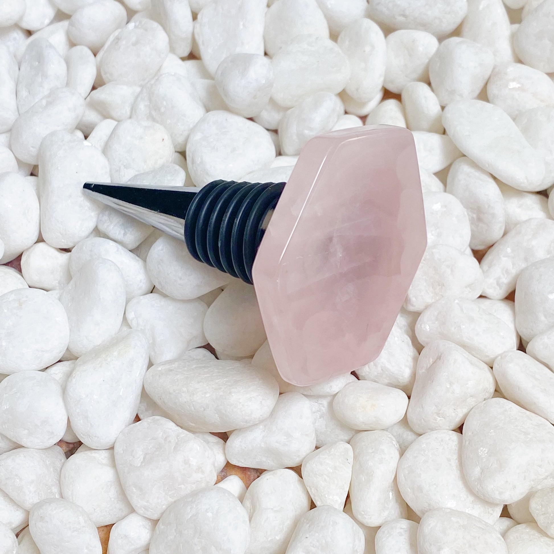 Pink bottle stopper with black cap on a bed of white pebbles
