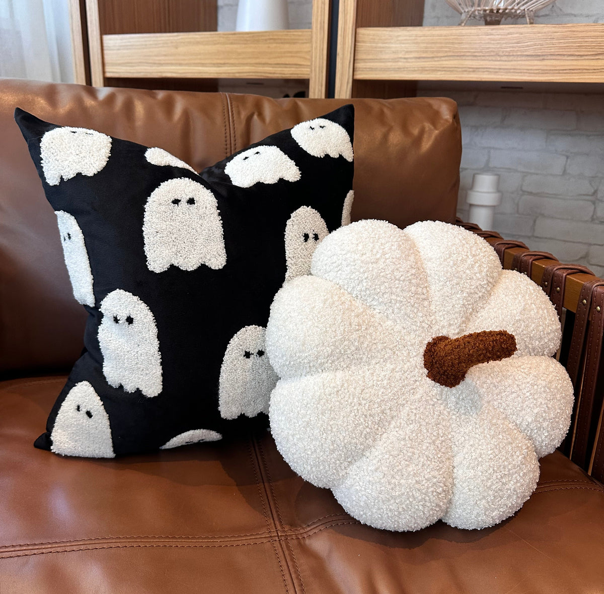 Decorative pillow with ghost pattern and pumpkin-shaped pillow on a brown leather couch.