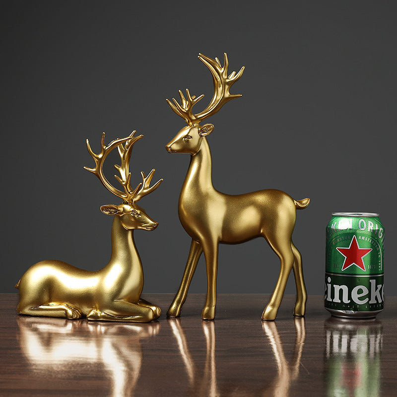 Two gold deer figurines next to a can of Heineken beer on a reflective surface with a dark background.