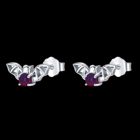 Pair of silver bat-shaped earrings with red gemstones on a white background