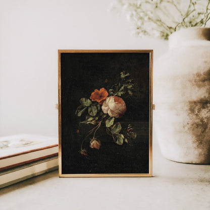 Floral painting in a gold frame on a white surface with a vase and books in the background.