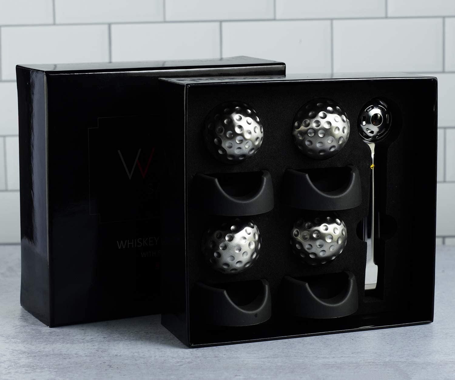 Black box with silver golf balls on a gray surface and tiled wall background