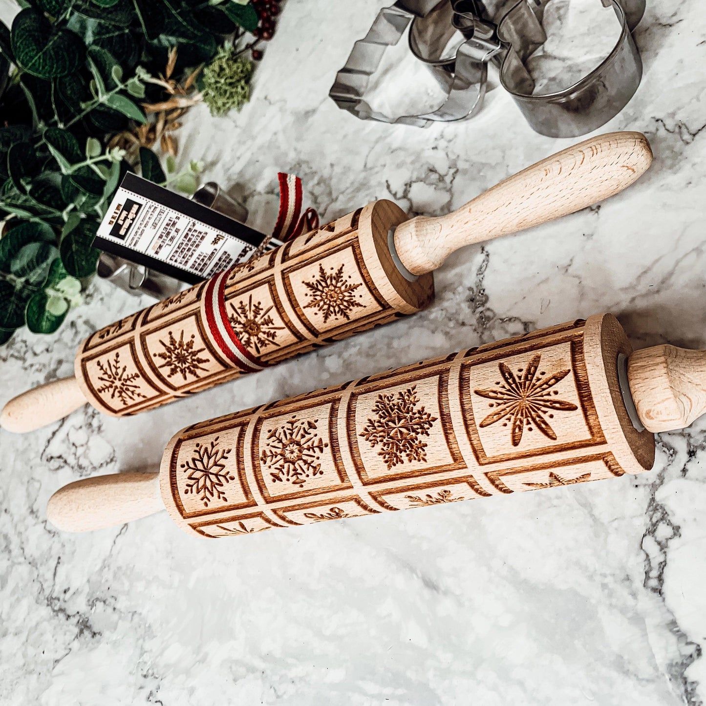 Two wooden rolling pins with engraved patterns on a marble surface.