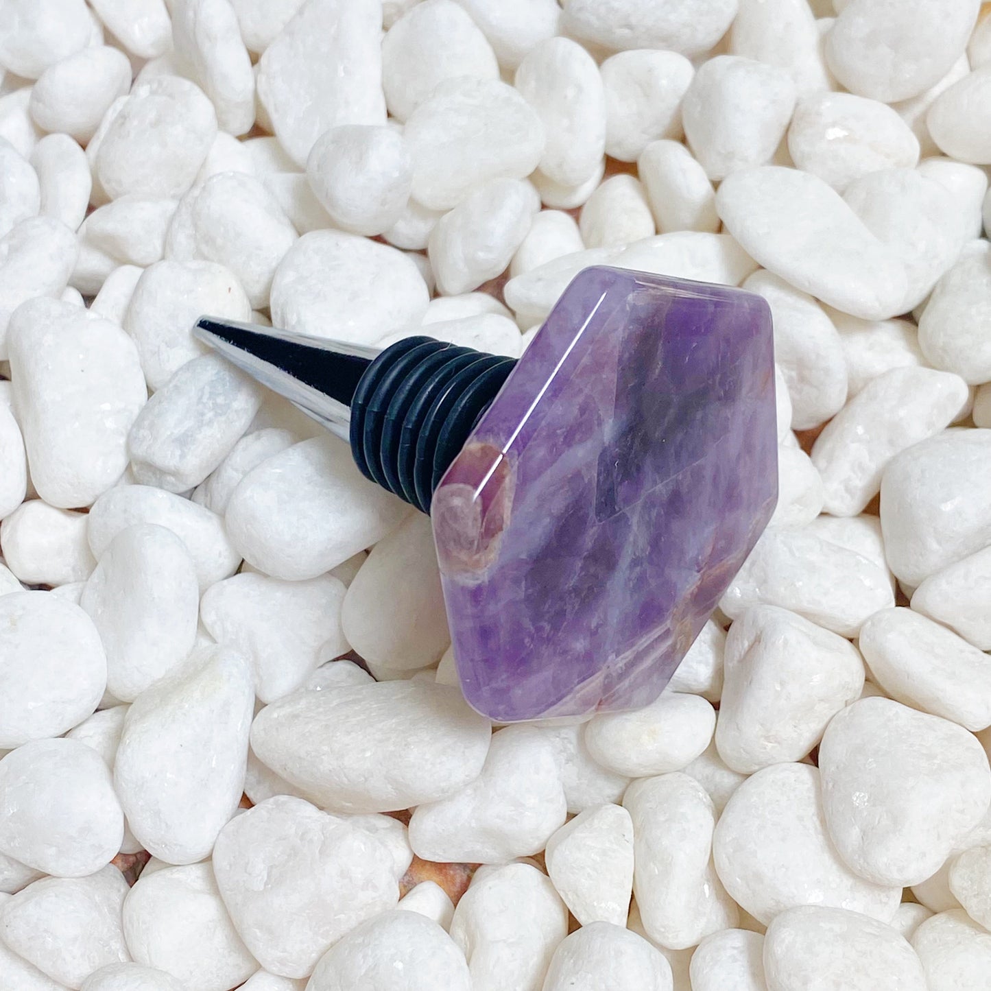 Purple gemstone wine stopper on white pebbles