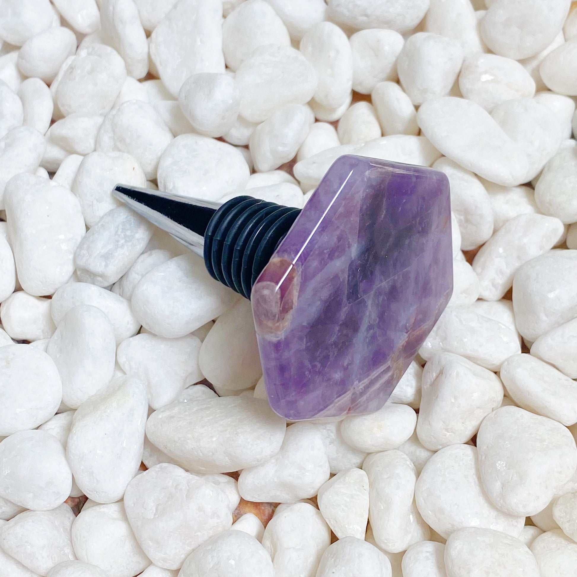 Purple gemstone wine stopper on white pebbles