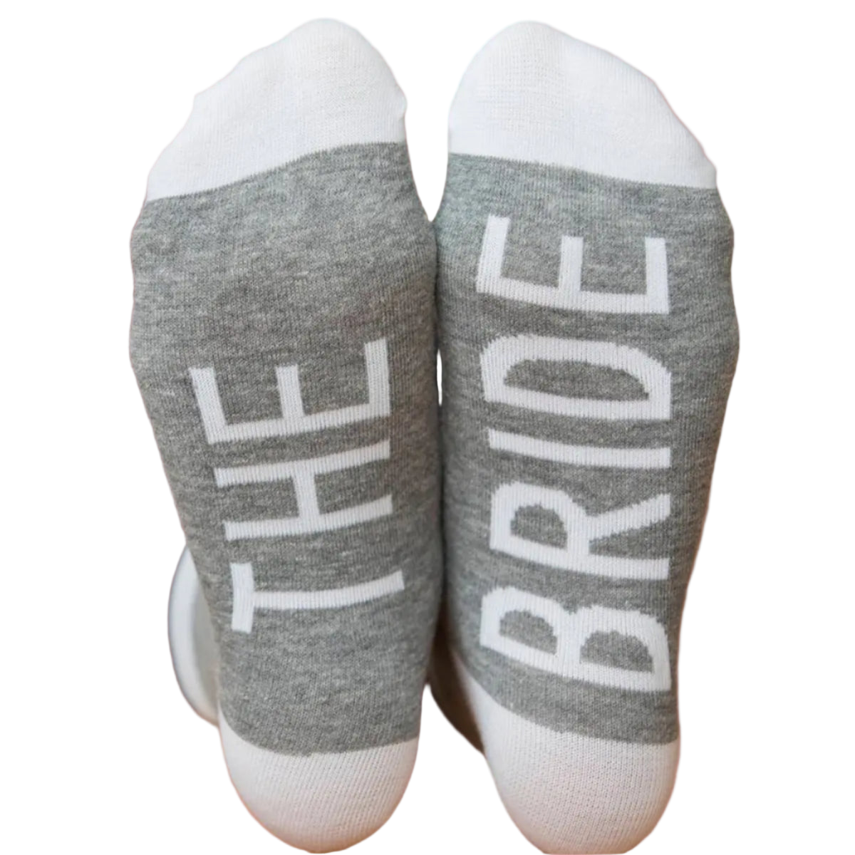 Gray socks with 'THE BRIDE' text on a wooden floor.