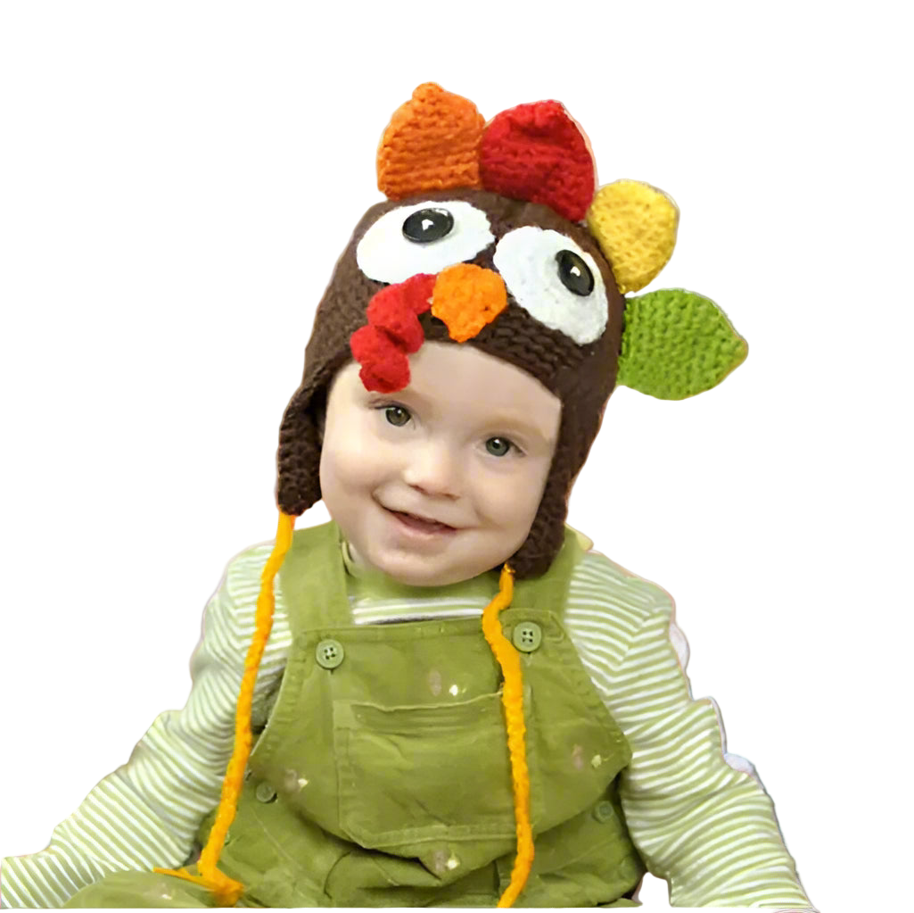 Child wearing a turkey-themed crochet hat with a colorful design, sitting in front of a blurred autumn background.