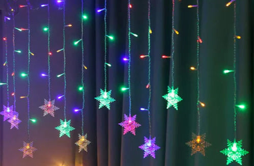 Decorative string lights shaped like snowflakes hanging against a dark curtain.