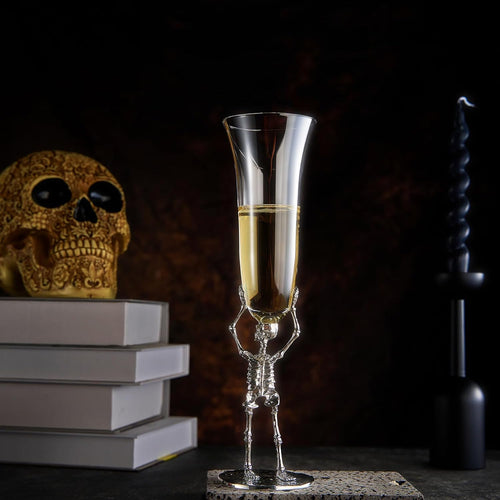 Skeletal champagne glass with champagne, skull, and books on a dark background