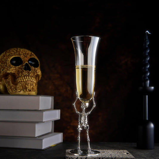 Skeletal champagne glass with champagne, skull, and books on a dark background