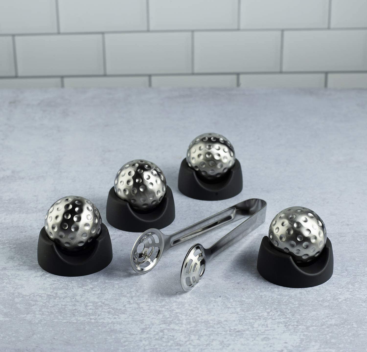 Set of metal ice ball molds with a tongs on a gray surface.