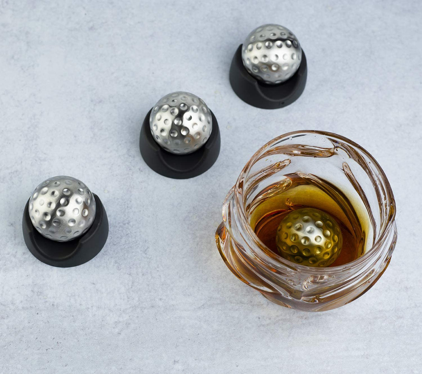 Metal ice balls in a glass of liquid on a light gray background